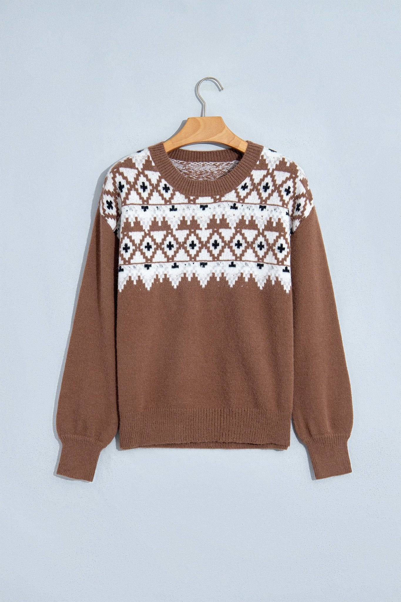 Brown knit sweater with white and black Fair Isle yoke pattern hanging on a wooden hanger.