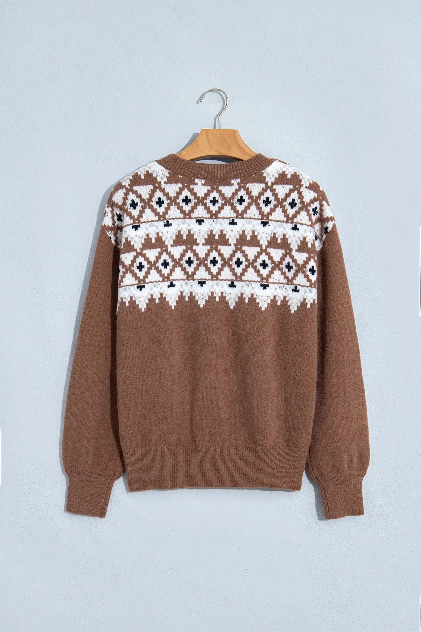 Brown knit sweater with white and black Fair Isle geometric yoke pattern on wooden hanger.