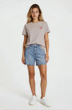 Woman wearing a gray t-shirt with a logo and denim shorts on a white background