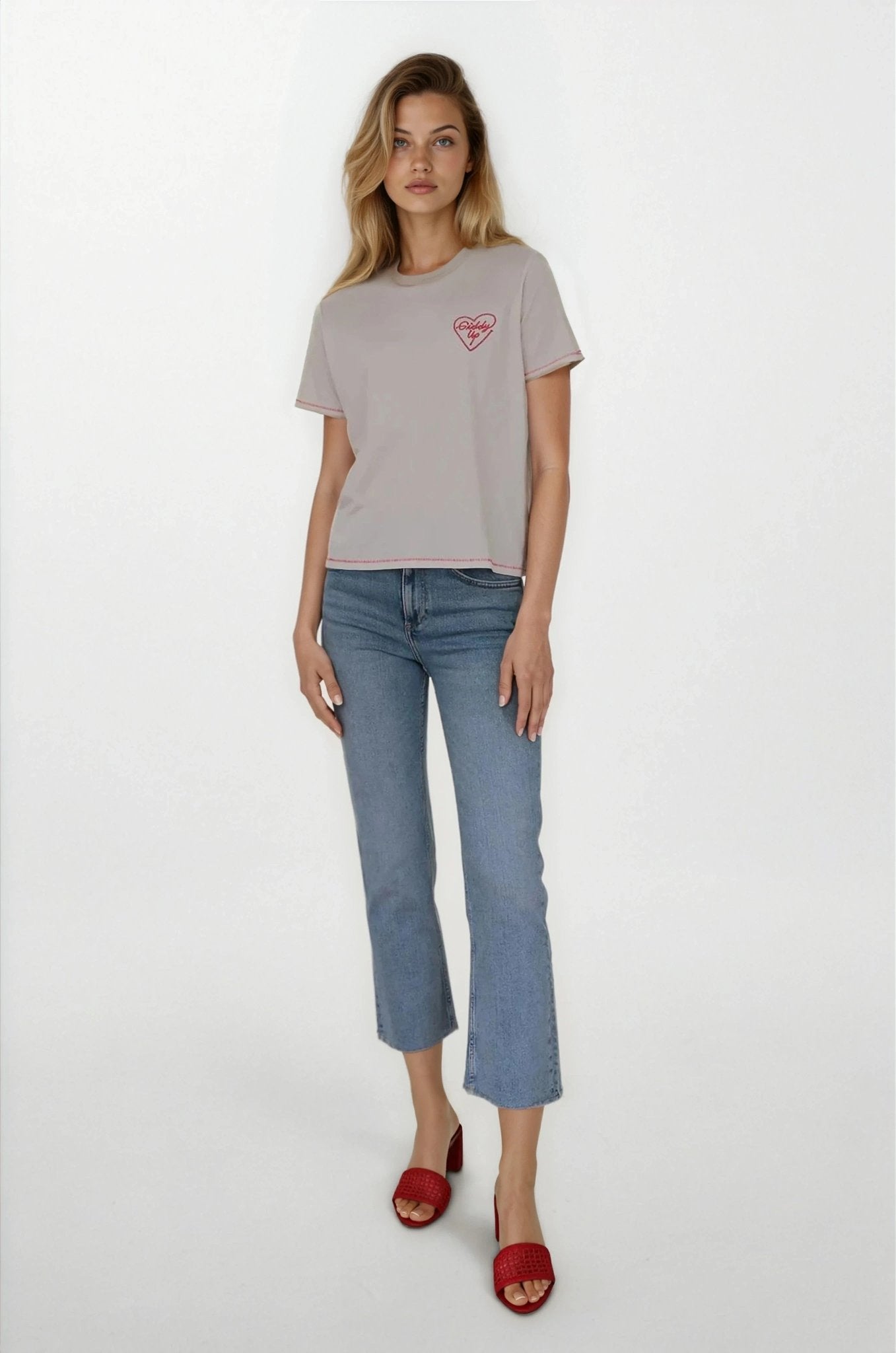 Woman wearing a gray t-shirt with a red logo and blue jeans on a white background