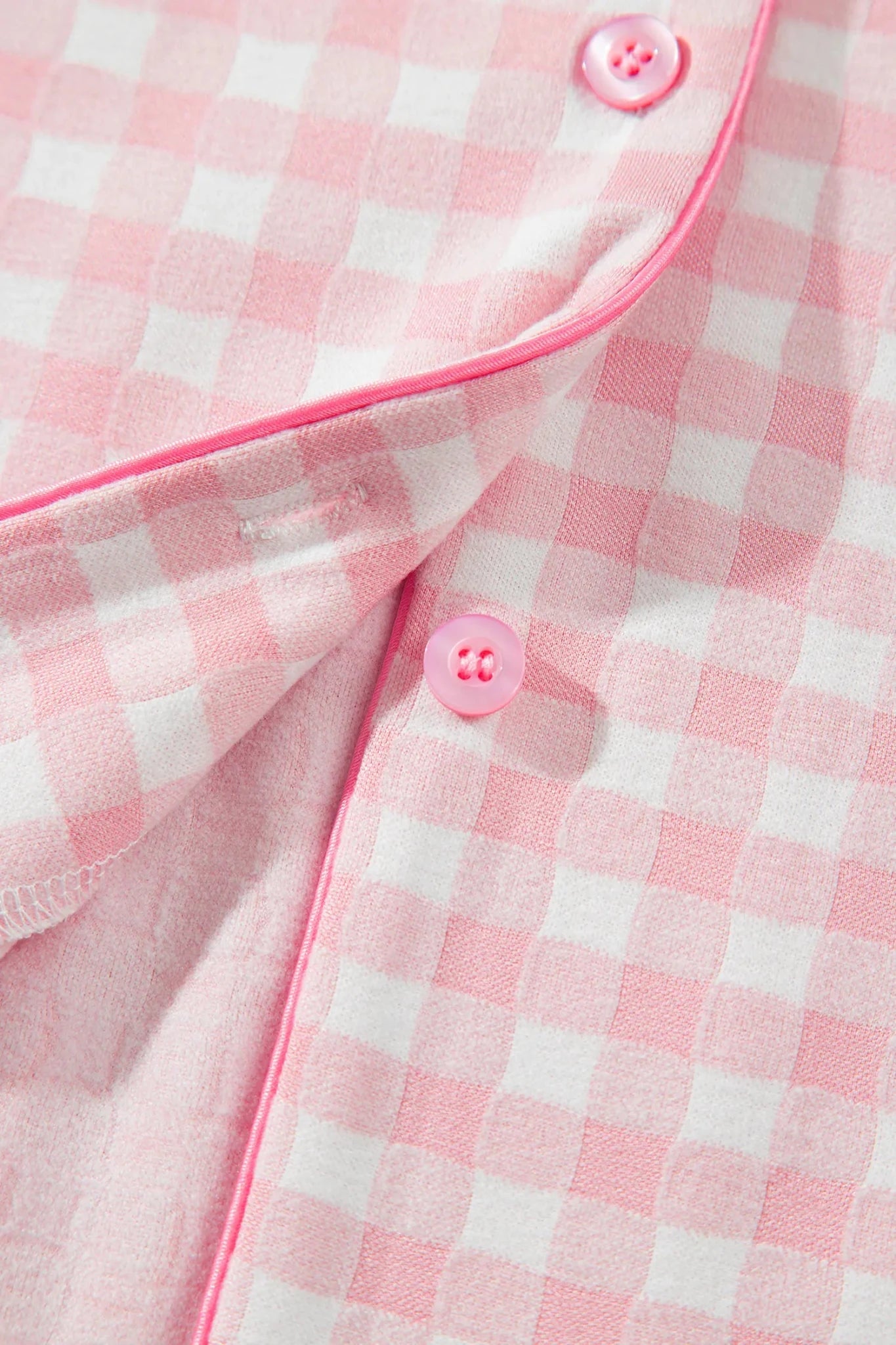 Close-up of a pink and white gingham pajama shirt with pink piping and matching pink buttons.