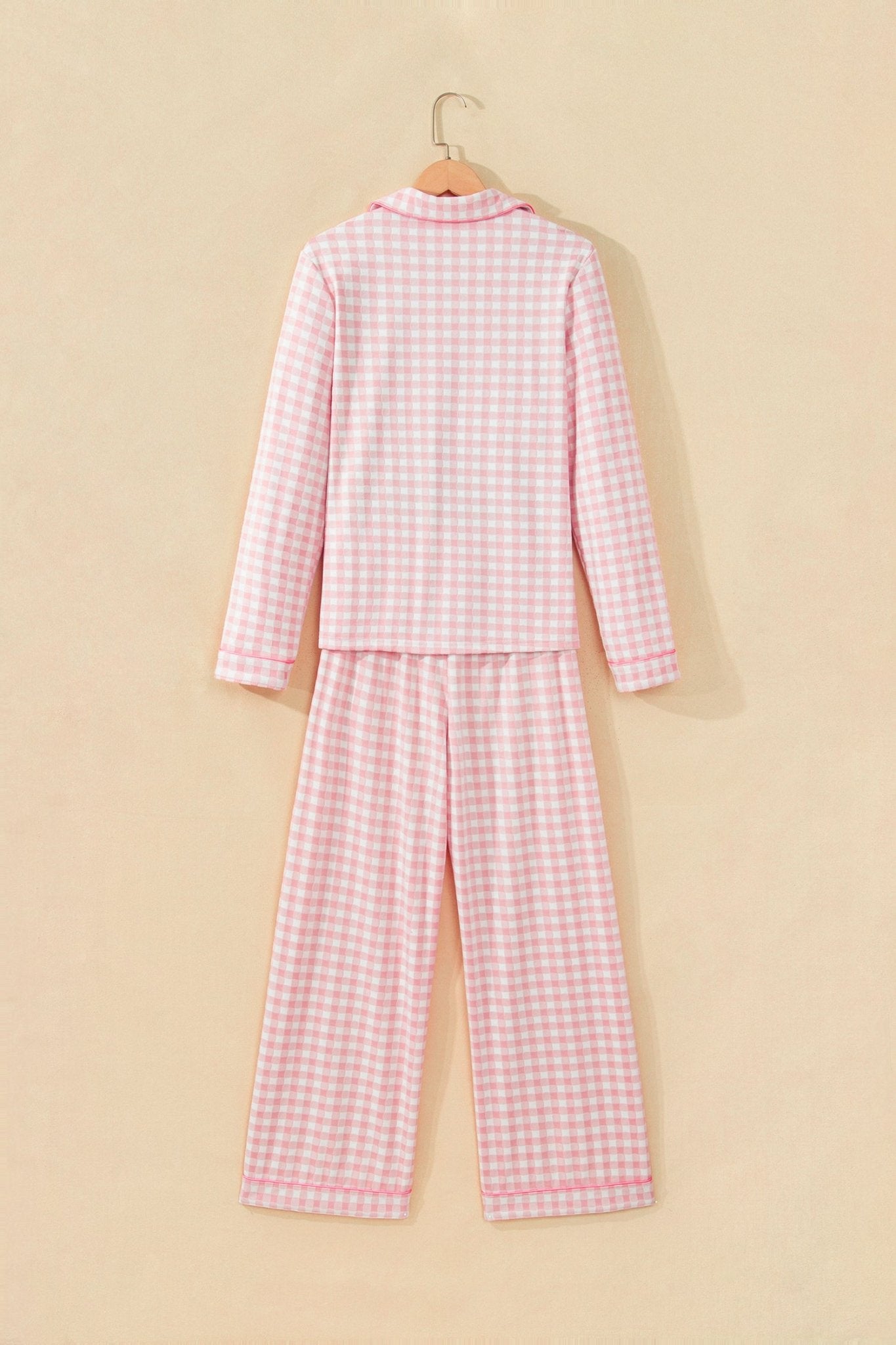 Pink-white gingham long-sleeve pajama set hanging on wooden hanger.