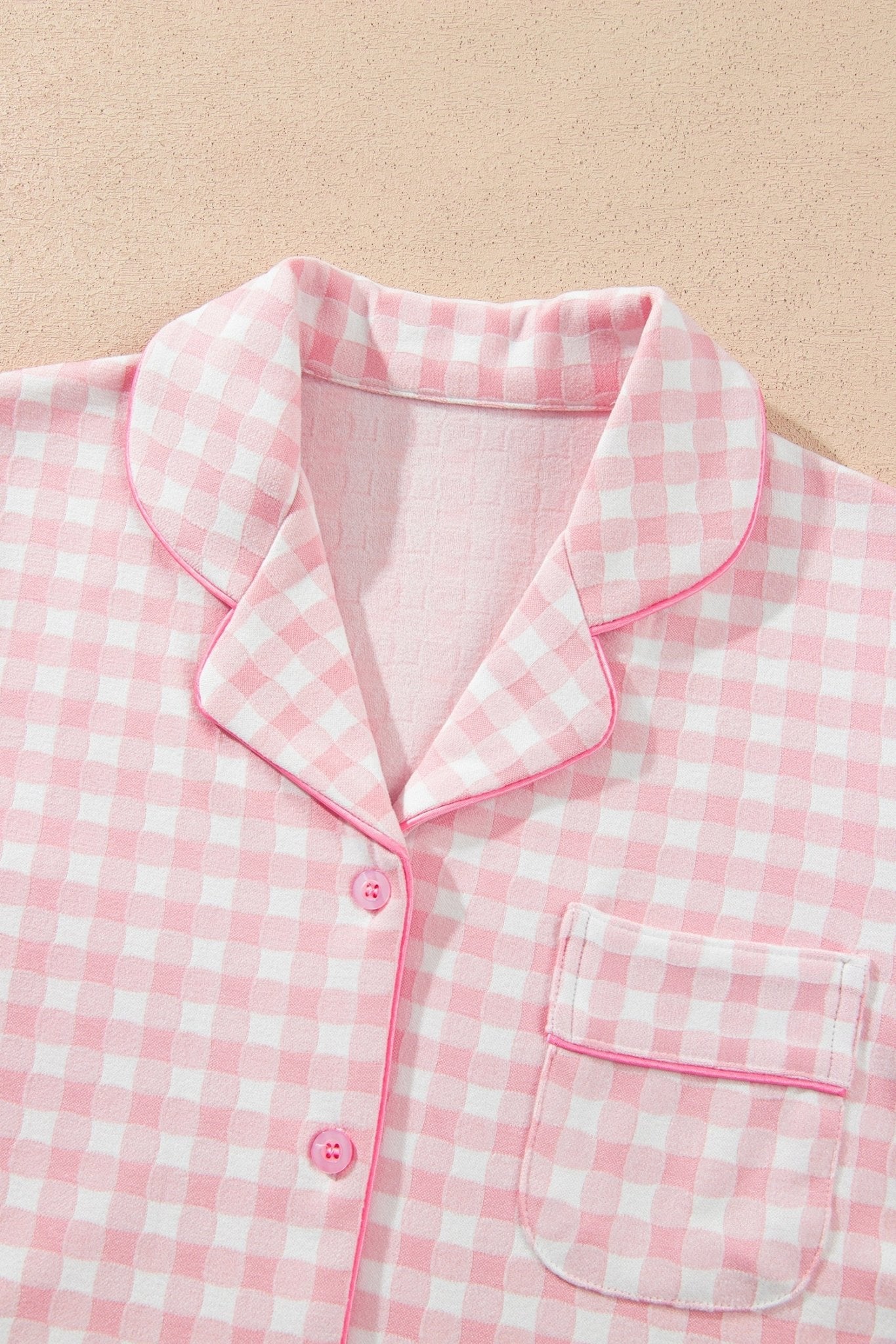 Pink-white gingham pajama top with pink piping and button placket, flat lay.