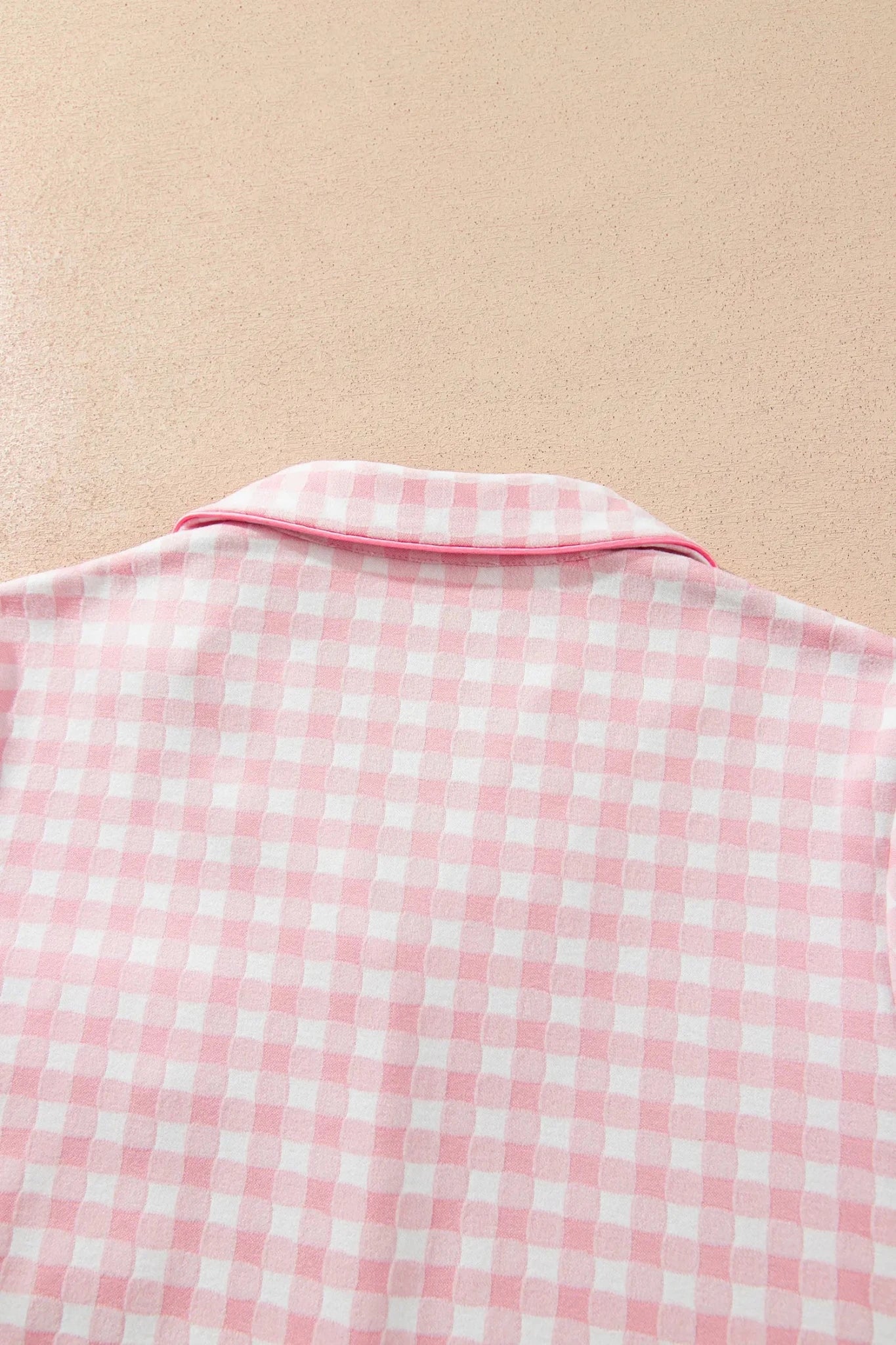 Pink-white gingham pajama top with solid pink collar, back view on beige background.