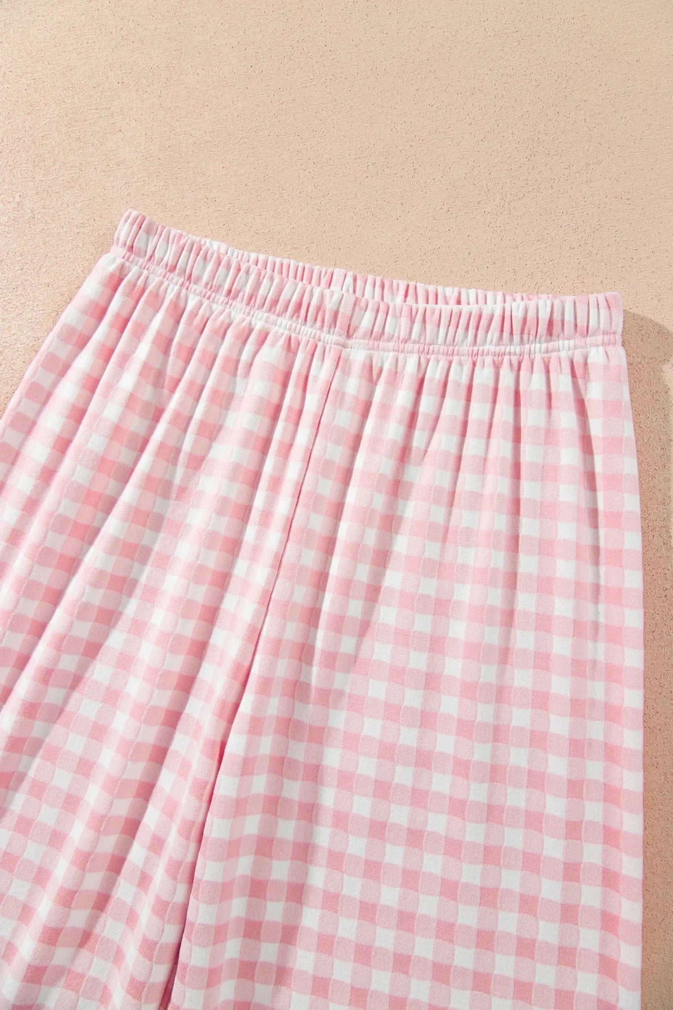 Pink-white gingham pants with elastic waistband, laid flat on beige background.