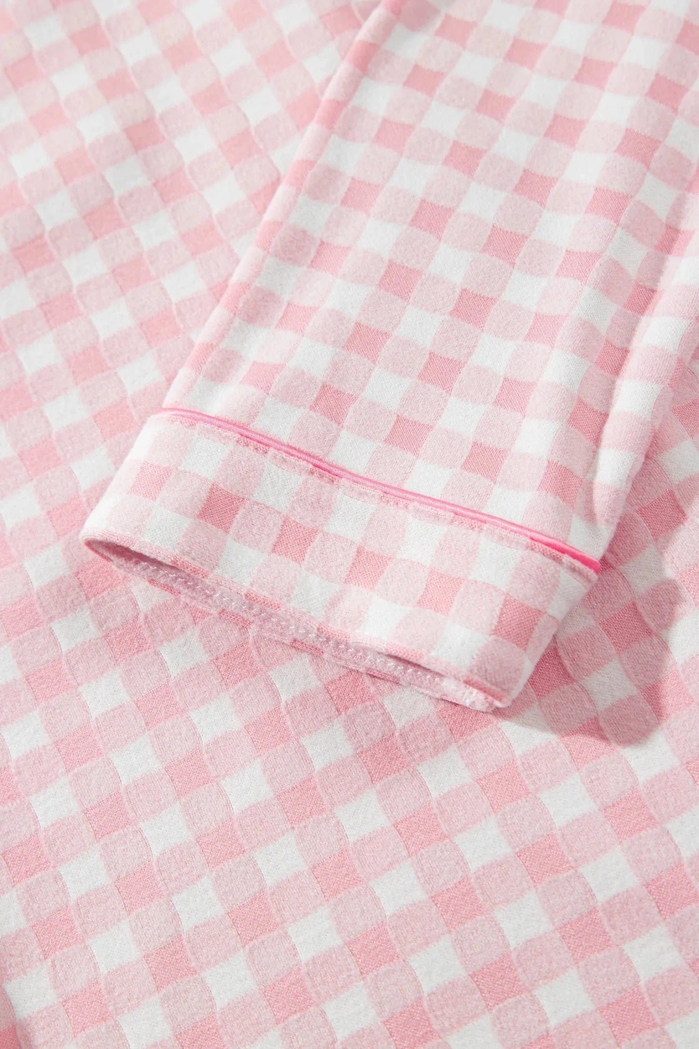 Close-up of pink-white gingham fabric with folded cuff and pink piping trim.