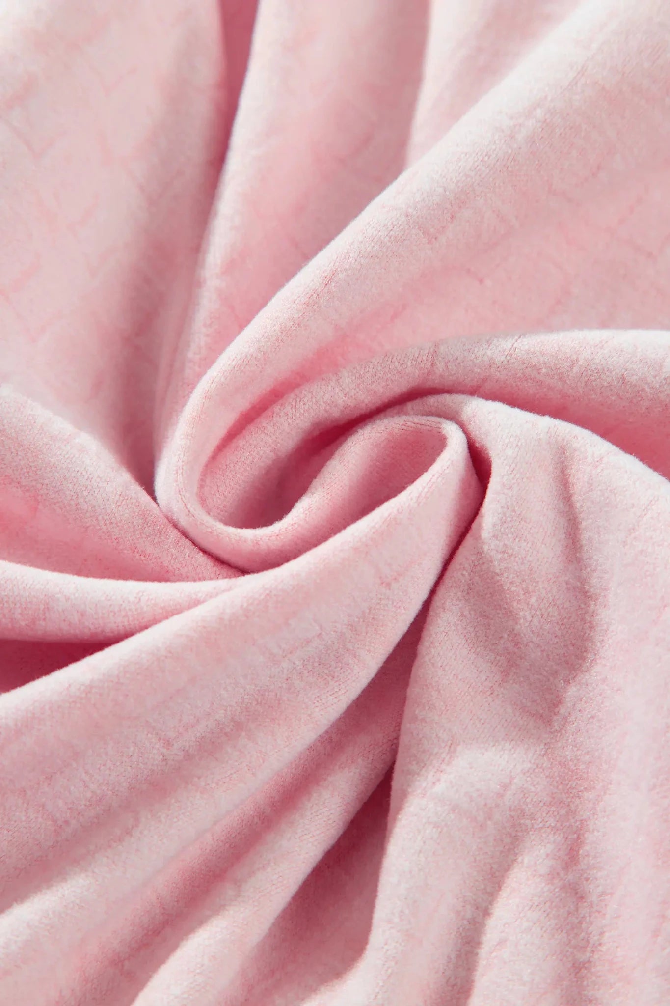 A close-up of soft pink fabric arranged in a spiral drape, showing the material texture and color.