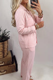 Woman in pink-white gingham pajamas taking a mirror selfie beside vintage suitcases.