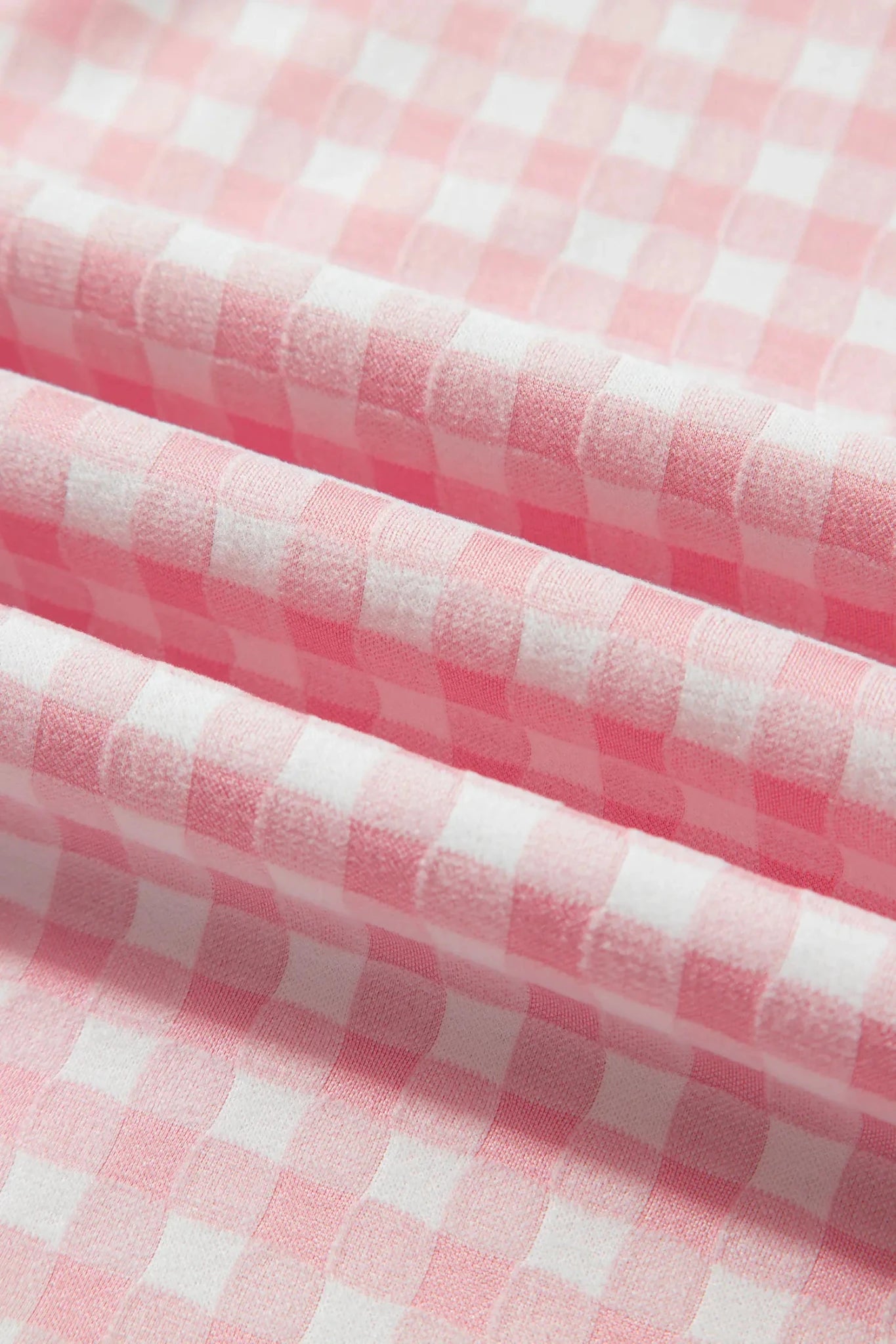 Pink and white gingham checkered fabric with soft folds showing its texture and pattern.