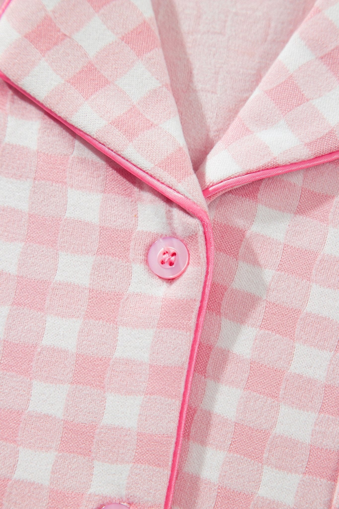 Close-up of pink-white gingham pajama top with pink piping and button.