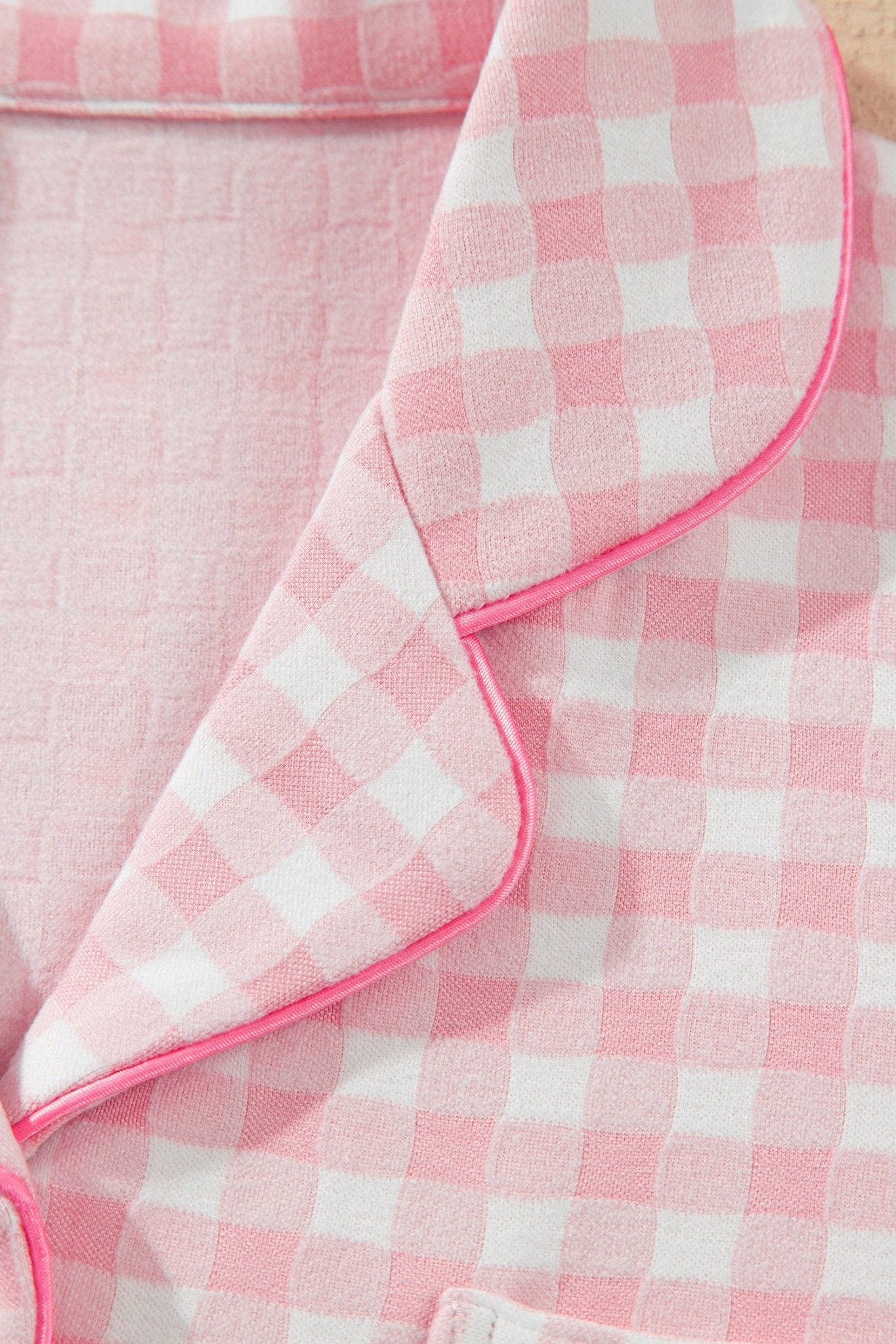 Close-up of pink-white gingham pajama top with collar, piping, and texture.
