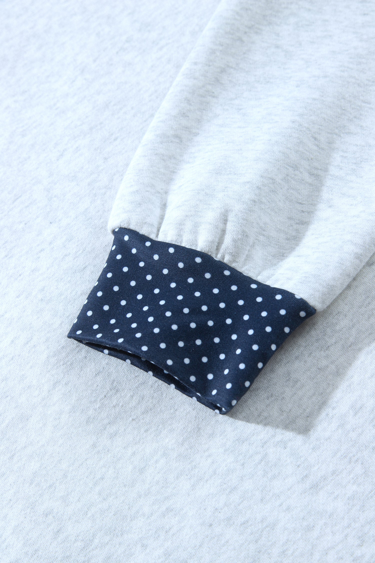 Navy polka dot cuff on gray sweatshirt sleeve, close-up