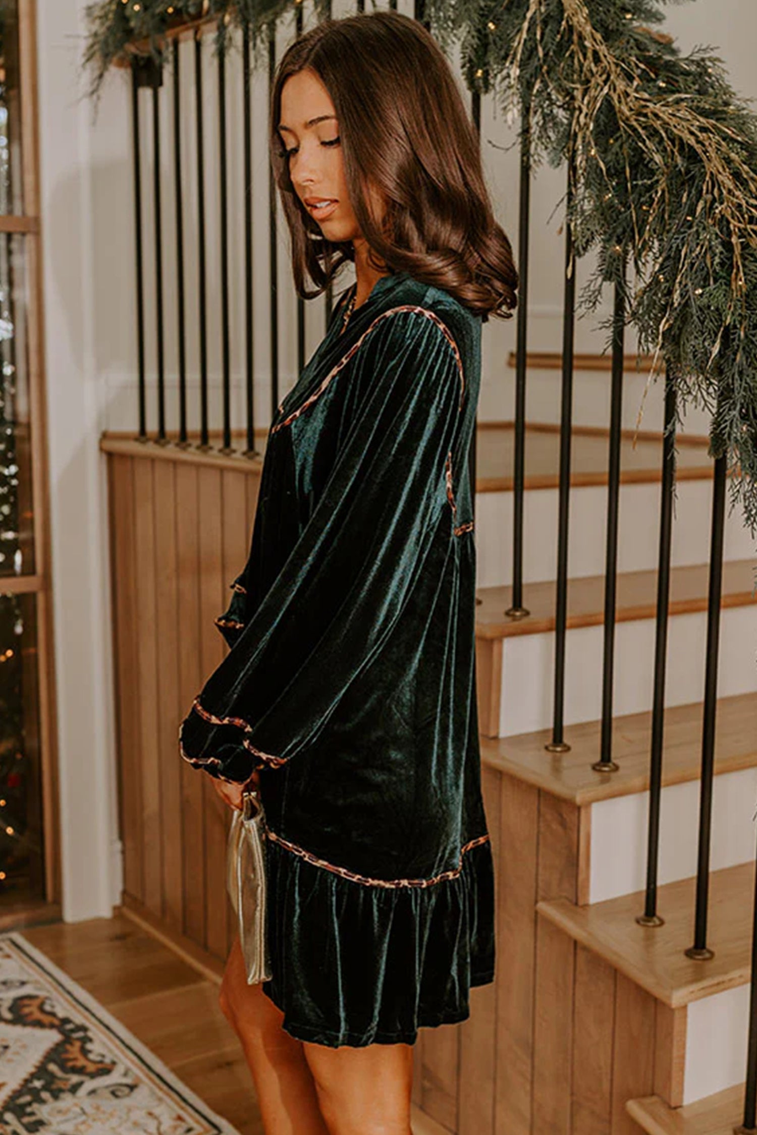 Woman in blackish green velvet leopard trim mini dress by a staircase