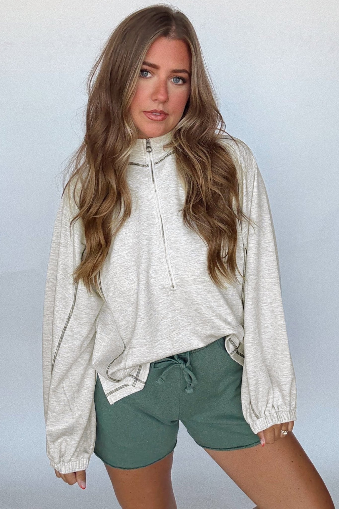 Woman wearing a light gray zip-up hoodie and green shorts against a plain background