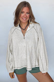 Woman wearing a light gray zip-up sweatshirt and green shorts against a plain background