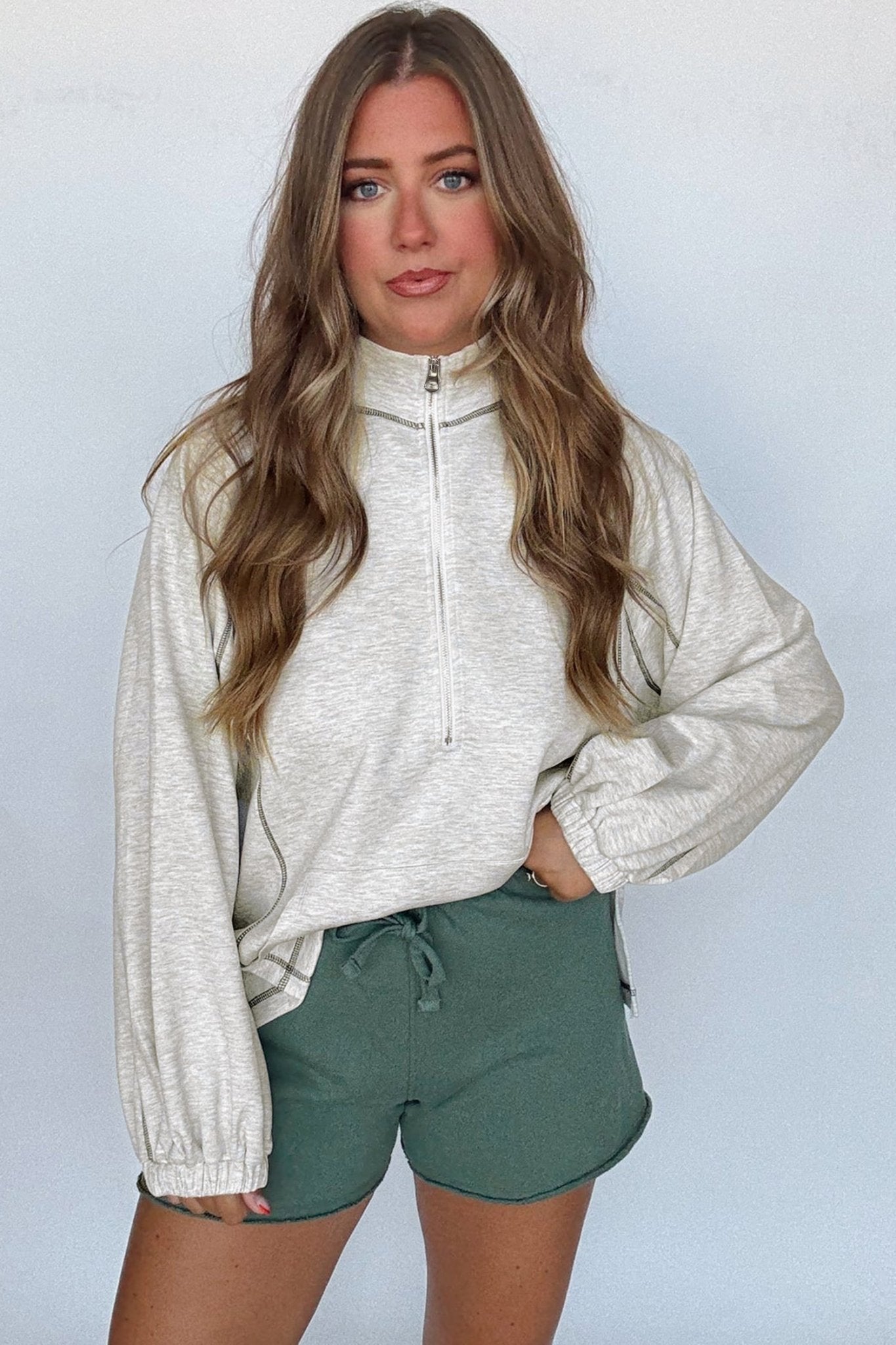 Woman wearing a light gray long-sleeve top and green shorts against a plain background