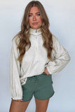 Woman wearing a light gray long-sleeve top and green shorts against a plain background
