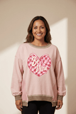 Woman wearing a pink sweatshirt with 'Be Mine' heart design against a beige background