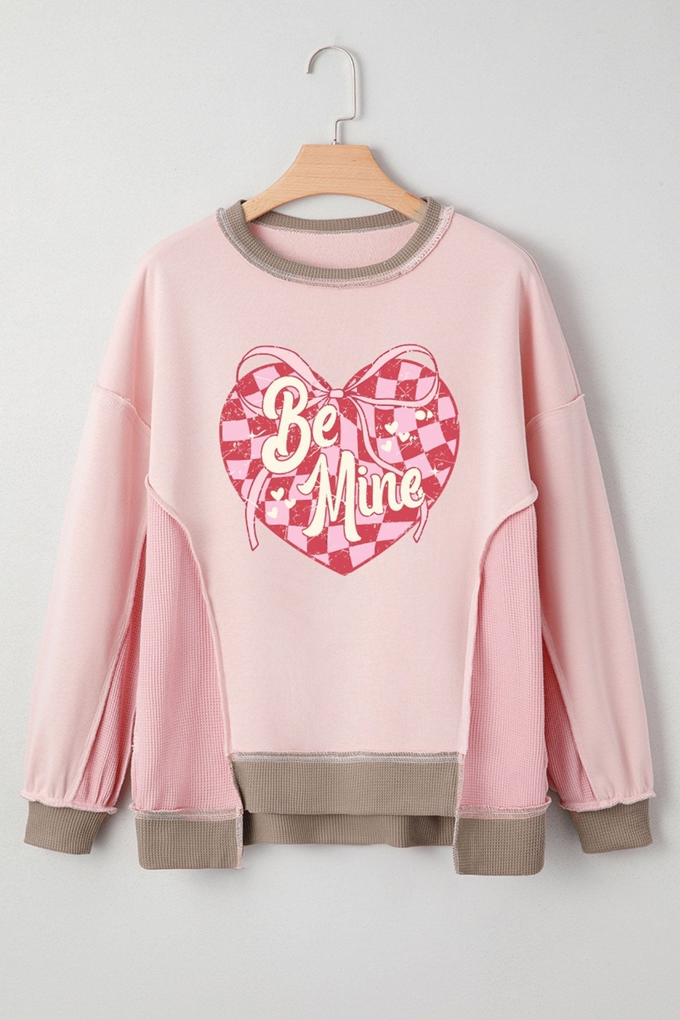 Pink sweatshirt with 'Be Mine' heart design on a hanger against a white background