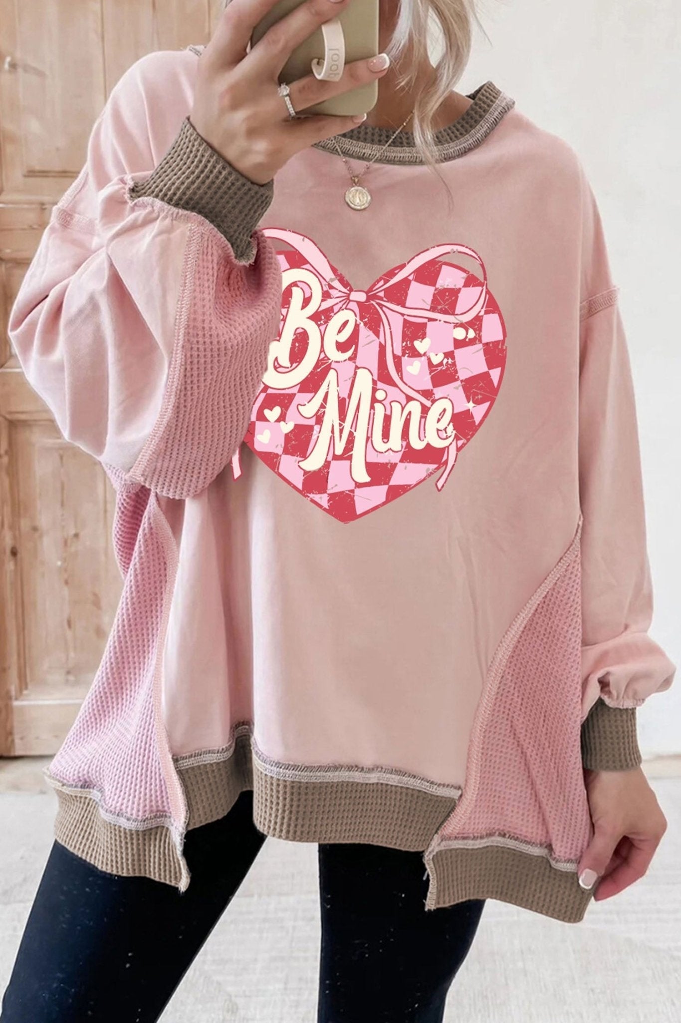 Person wearing a pink sweatshirt with a heart design and 'Be Mine' text.