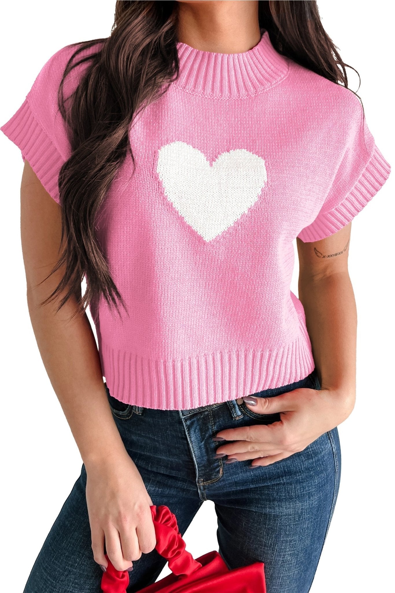 Pink sweater with a white heart design worn by a person, holding red shoes.