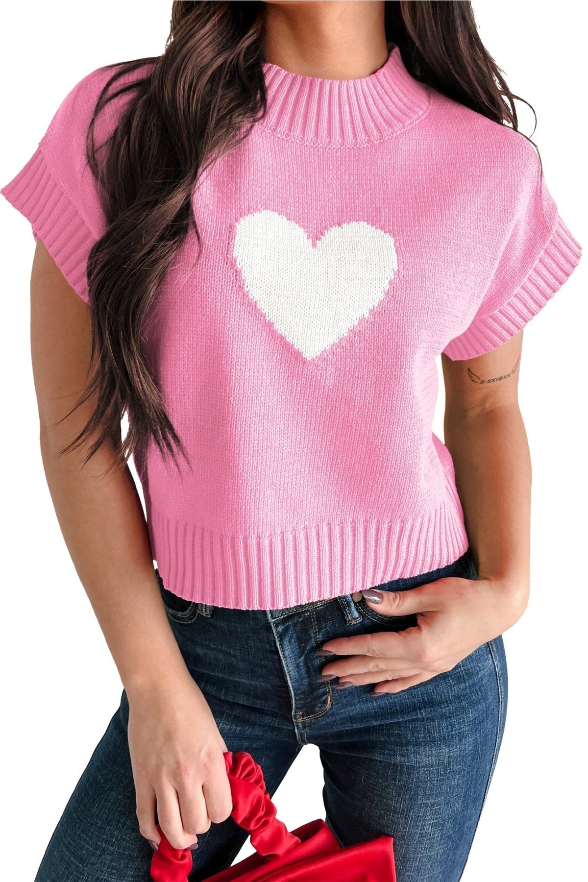 Pink sweater with a white heart design worn by a person, holding red shoes.