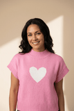 Woman wearing a pink sweater with a white heart design against a beige background