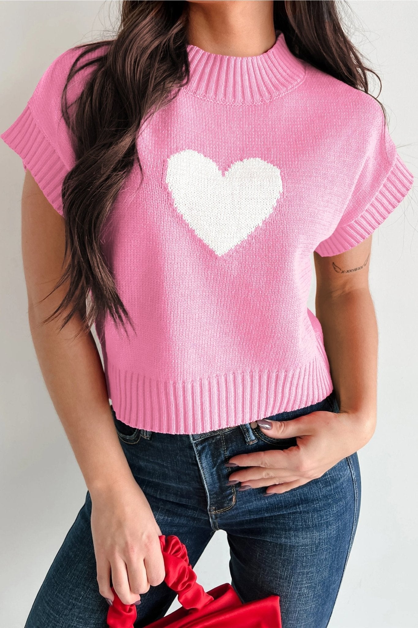 Person wearing a pink sweater with a white heart design on a plain background