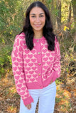 Woman in pink heart-patterned cardigan with gold-tone buttons outdoors.