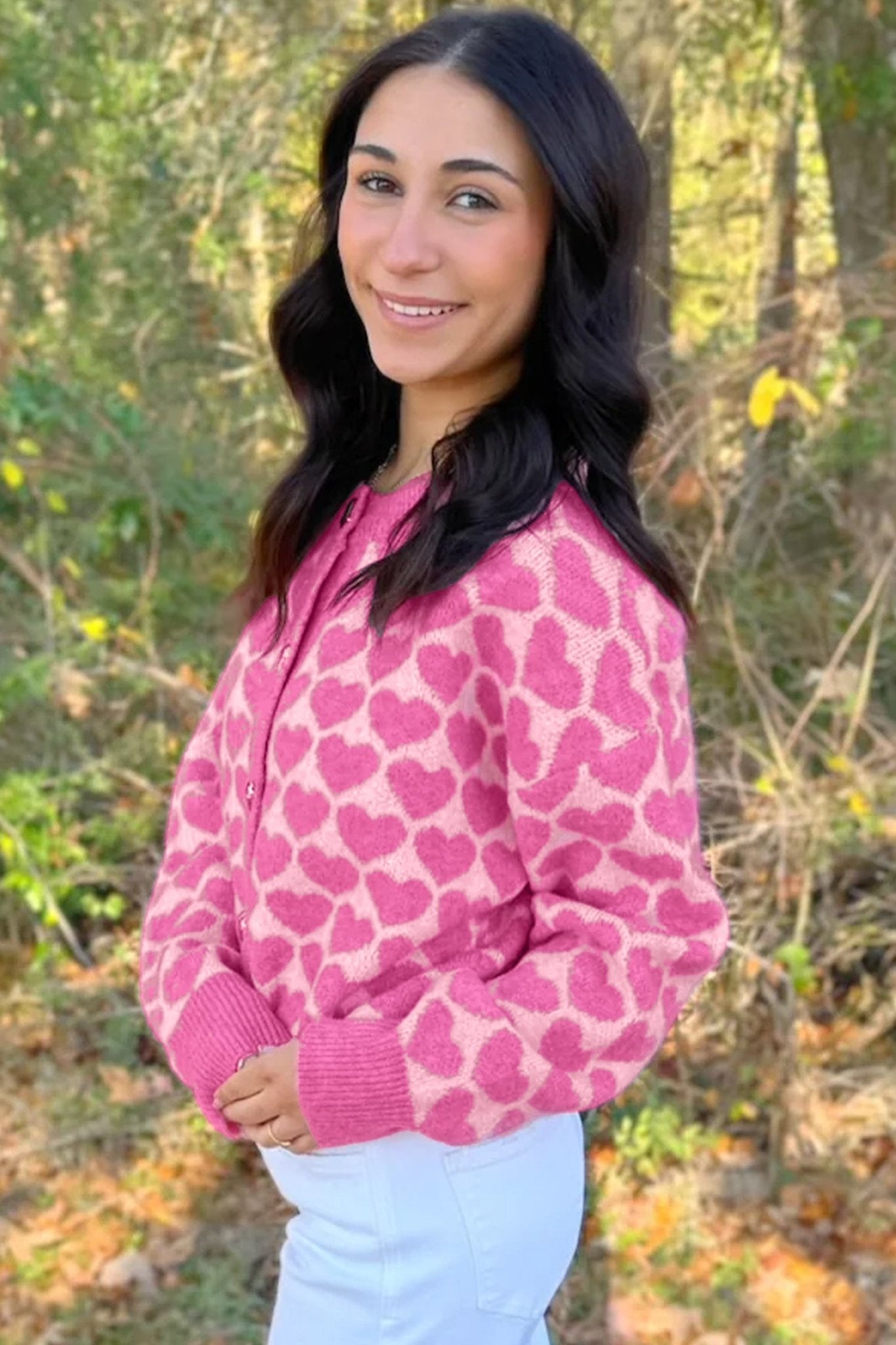 Woman in pink heart-patterned cardigan with white pants, outdoors.
