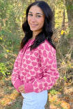 Woman in pink heart-patterned cardigan with white pants, outdoors.
