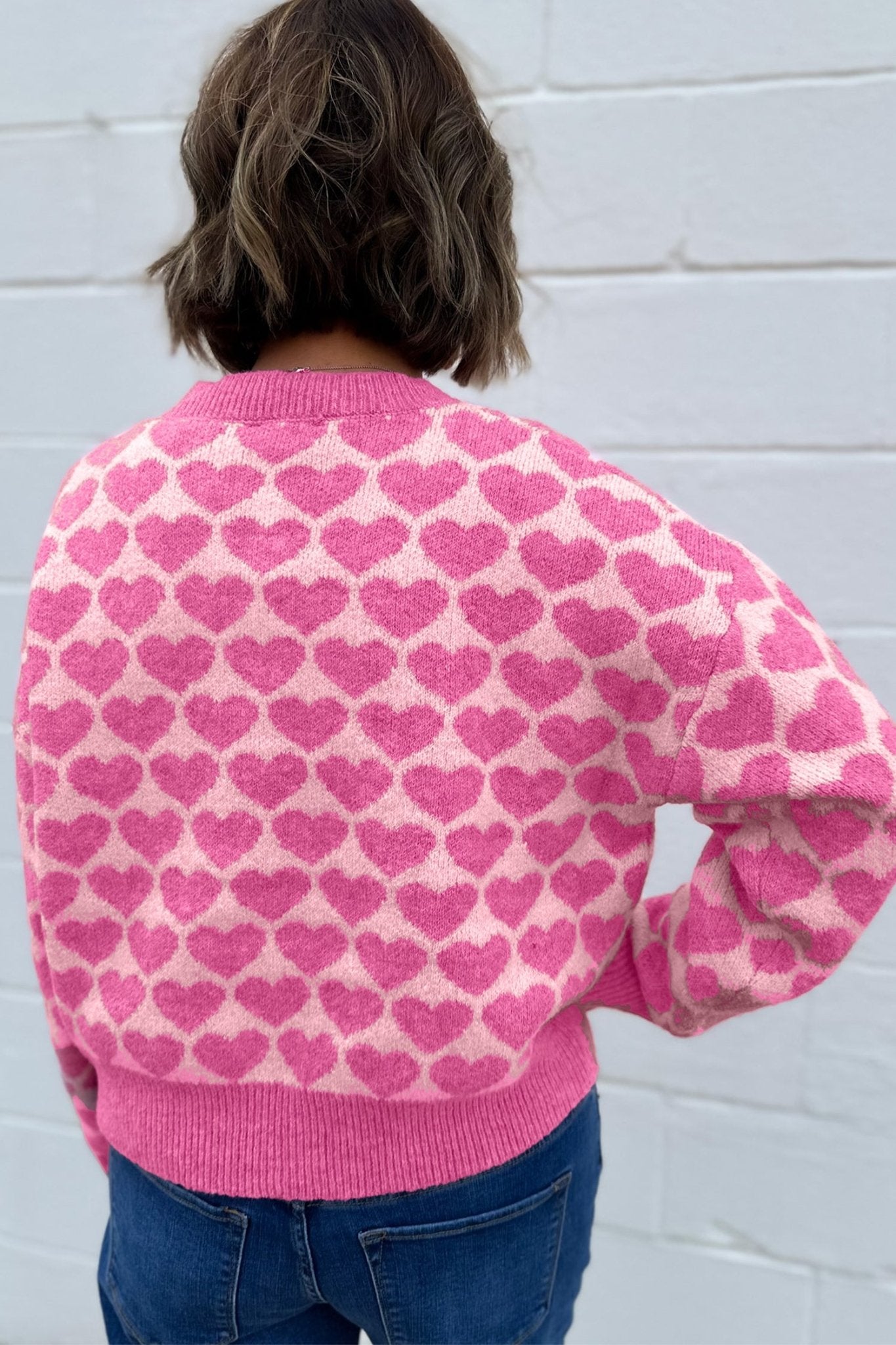 Back view of person in pink heart-patterned sweater with blue jeans.