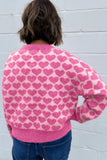Back view of person in pink heart-patterned sweater with blue jeans.