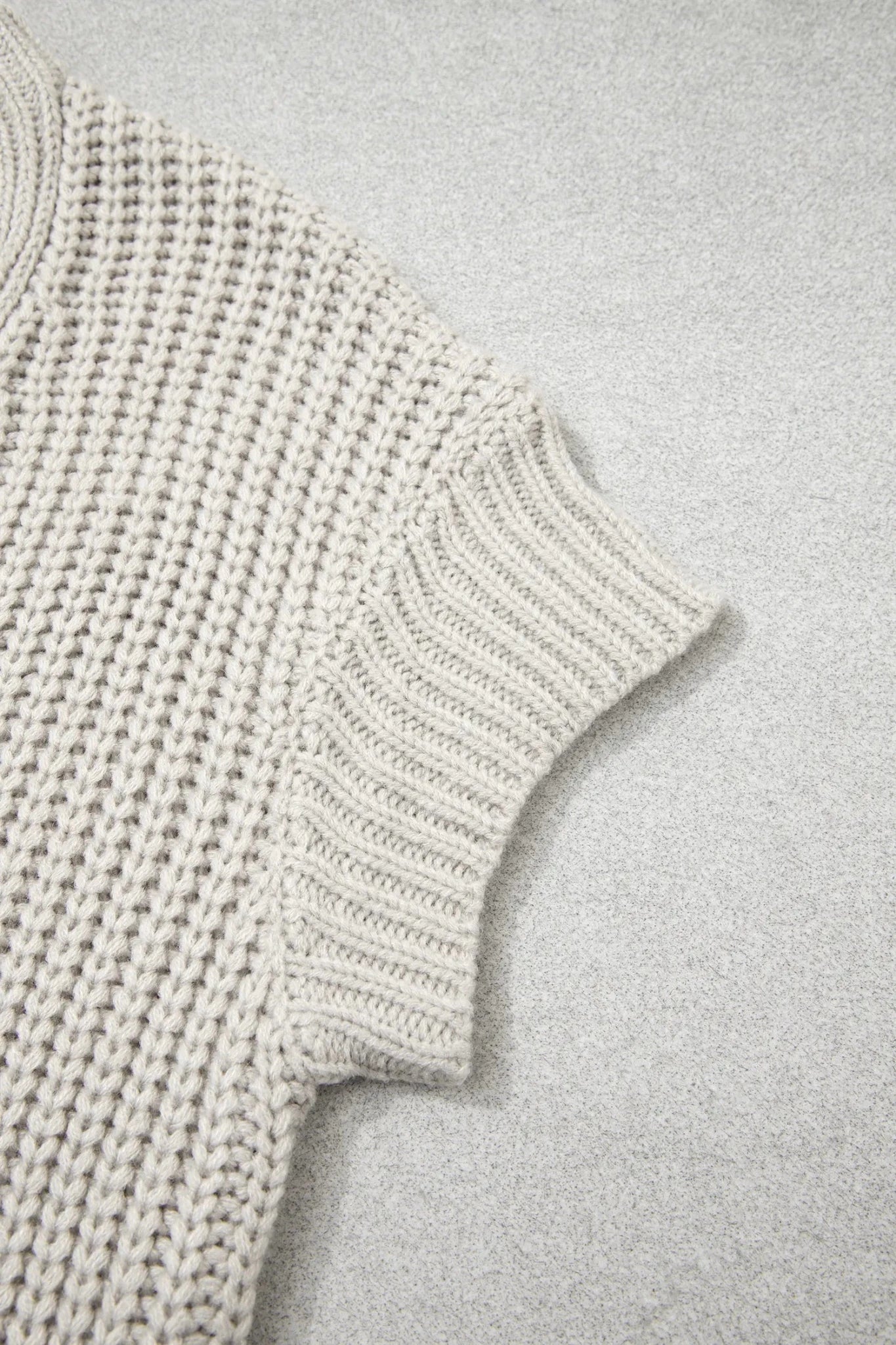 Close-up of a light oatmeal chunky knit sweater with ribbed sleeve cuff.