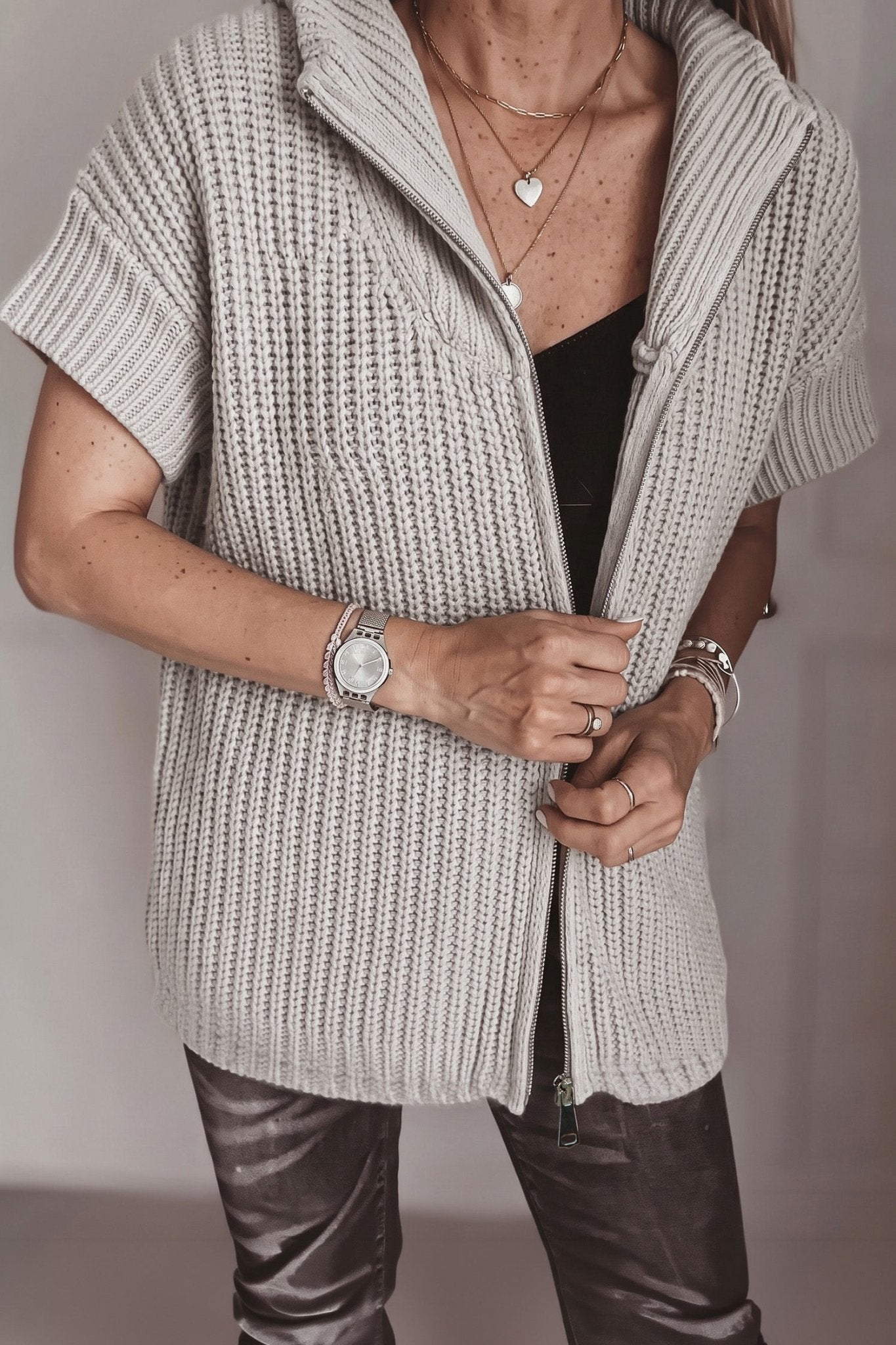Woman wearing a light gray waffle-knit zip vest over a black top and dark pants.
