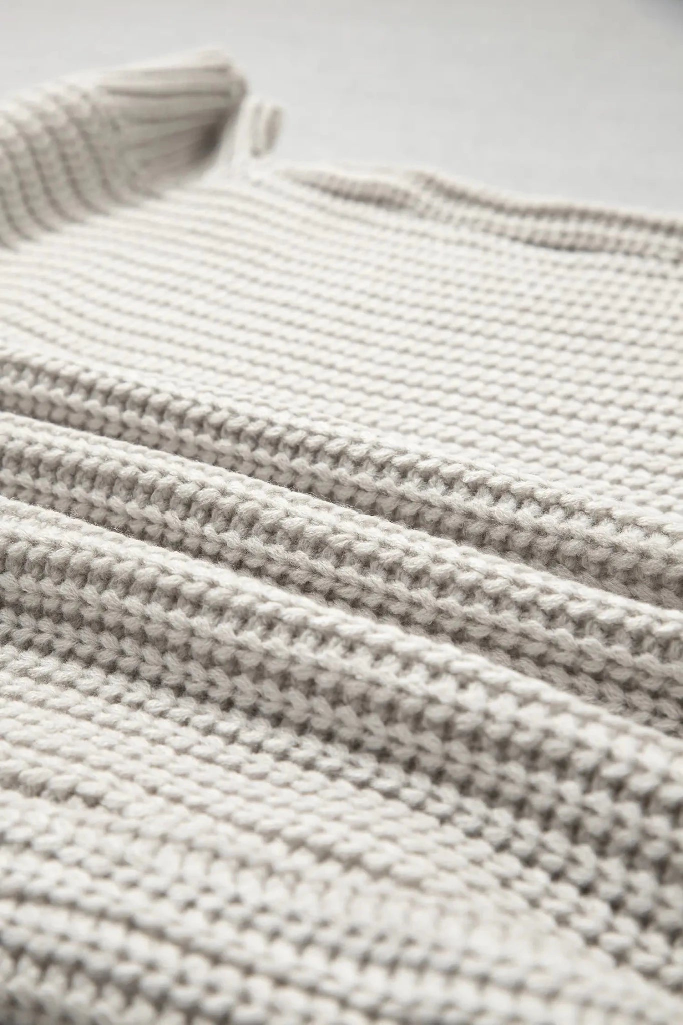 Close-up of a light oatmeal chunky knit sweater with a ribbed folded collar.