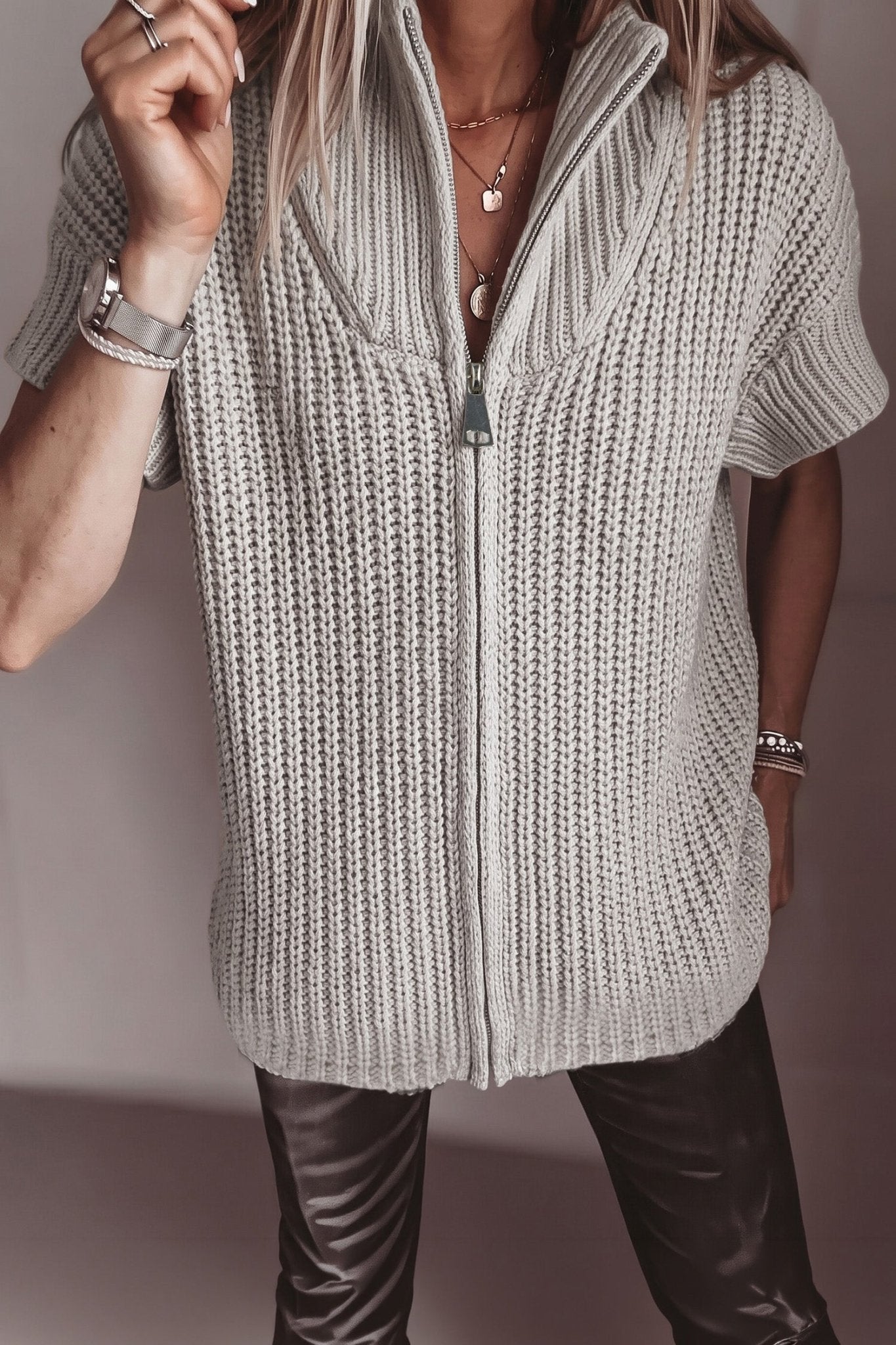 Person wearing a light gray chunky knit zip cardigan with high collar and leather pants.