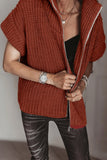 Person wearing a rust-orange chunky knit zip cardigan over a black top and dark gray jeans.