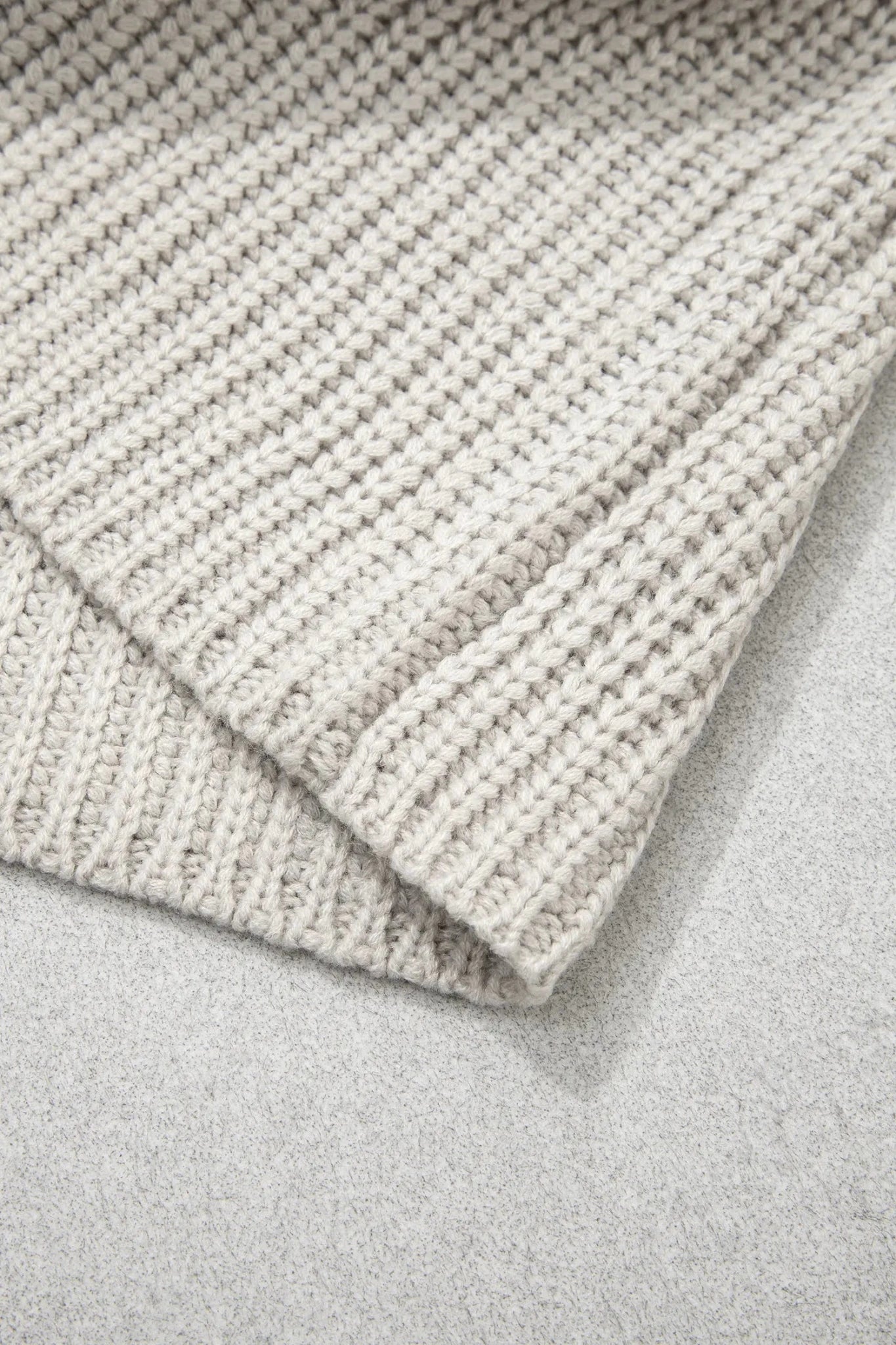 Close-up of warm gray chunky knit textile with a folded ribbed edge.