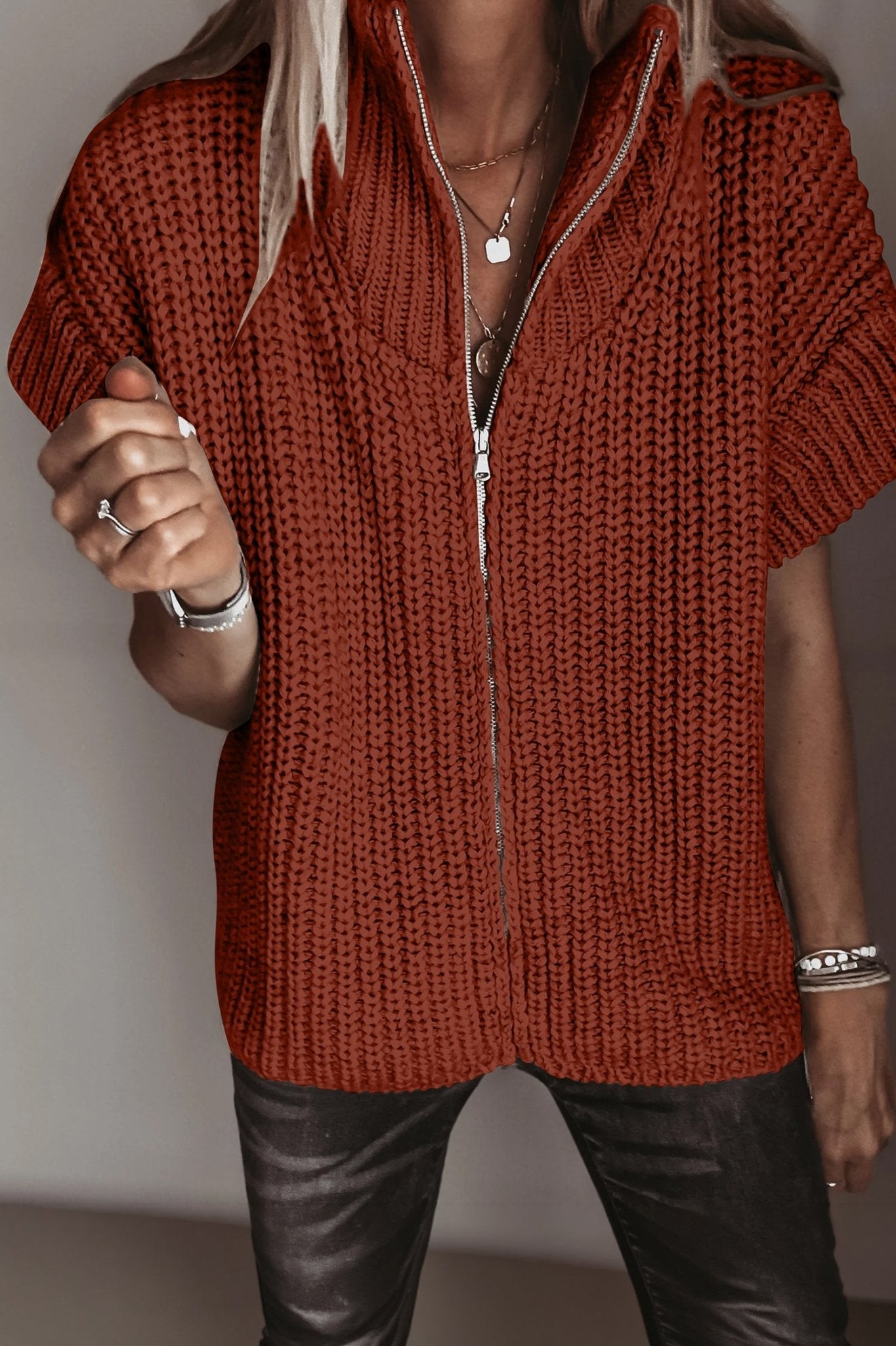Woman wearing a rust-orange chunky knit sweater with short sleeves and black leather pants.