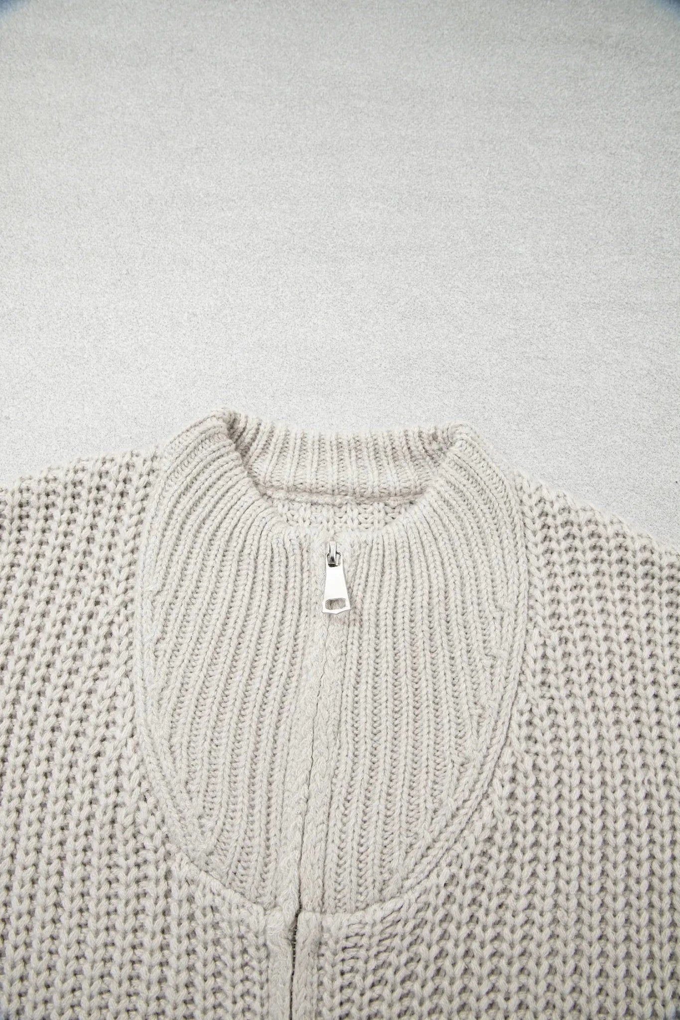 Close-up of a light oatmeal chunky knit sweater with ribbed collar and silver zipper.