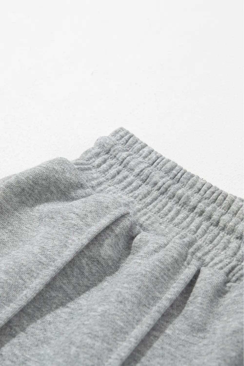 Close-up of light gray heathered fabric with ribbed elastic waistband and folds.
