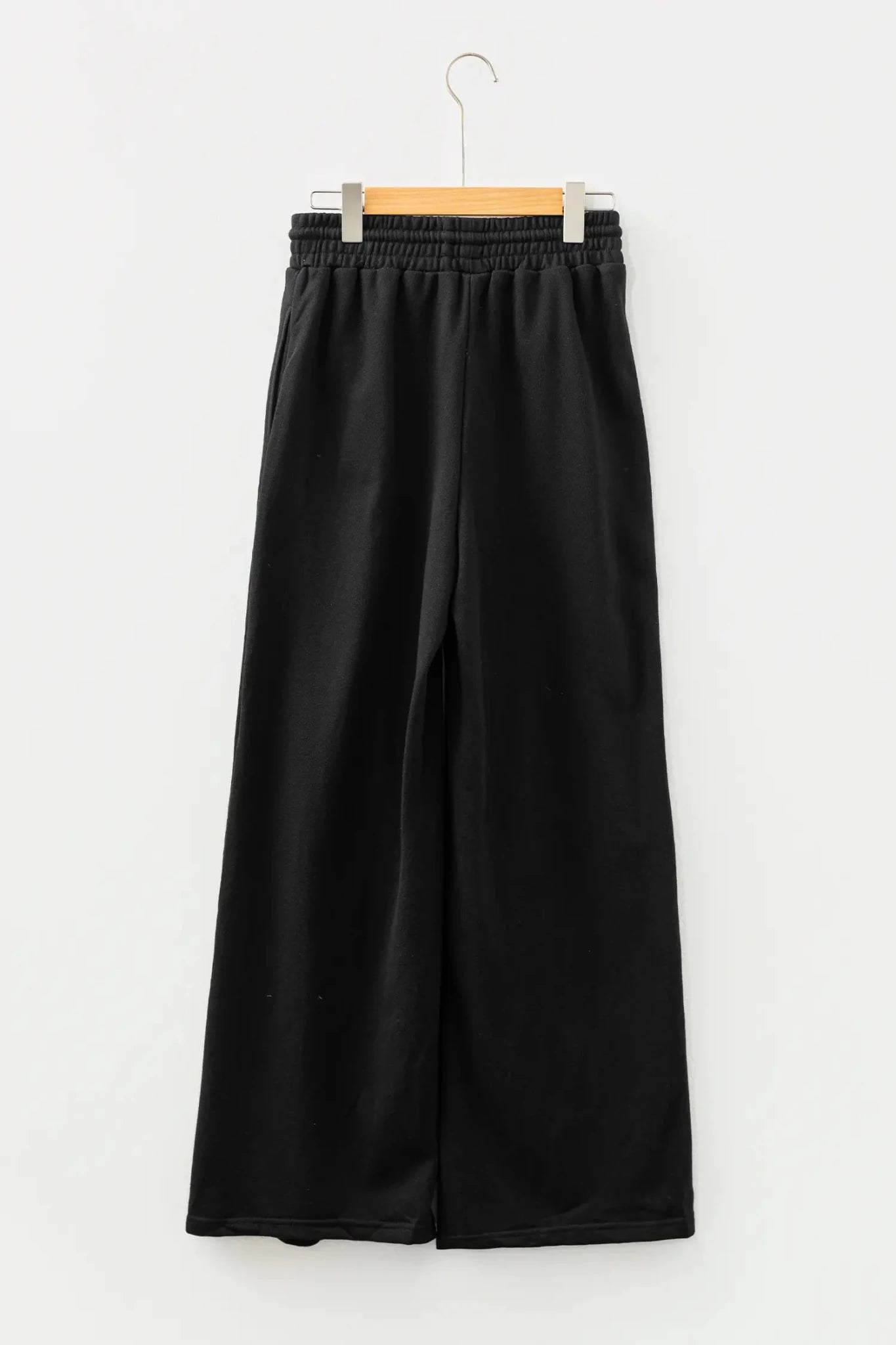Black wide-leg cropped pants with elastic waistband hanging on wooden hanger.