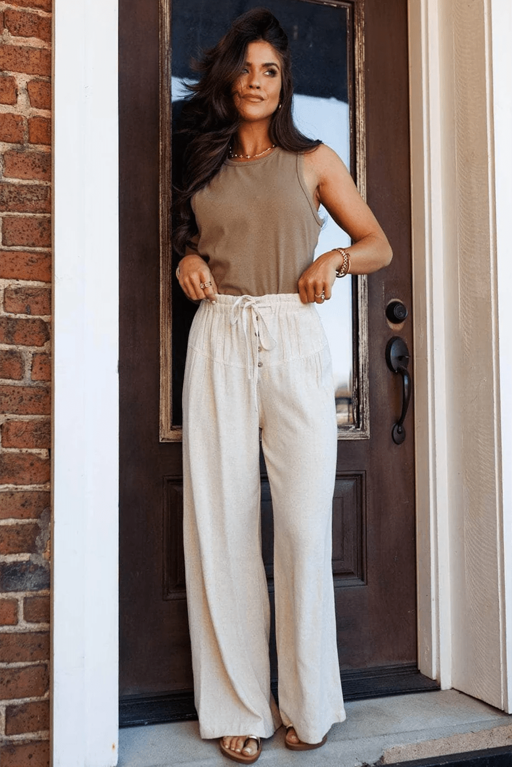 Woman wearing a brown top and white pants standing in front of a door.