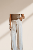 Person wearing a beige top and white pants against a neutral background
