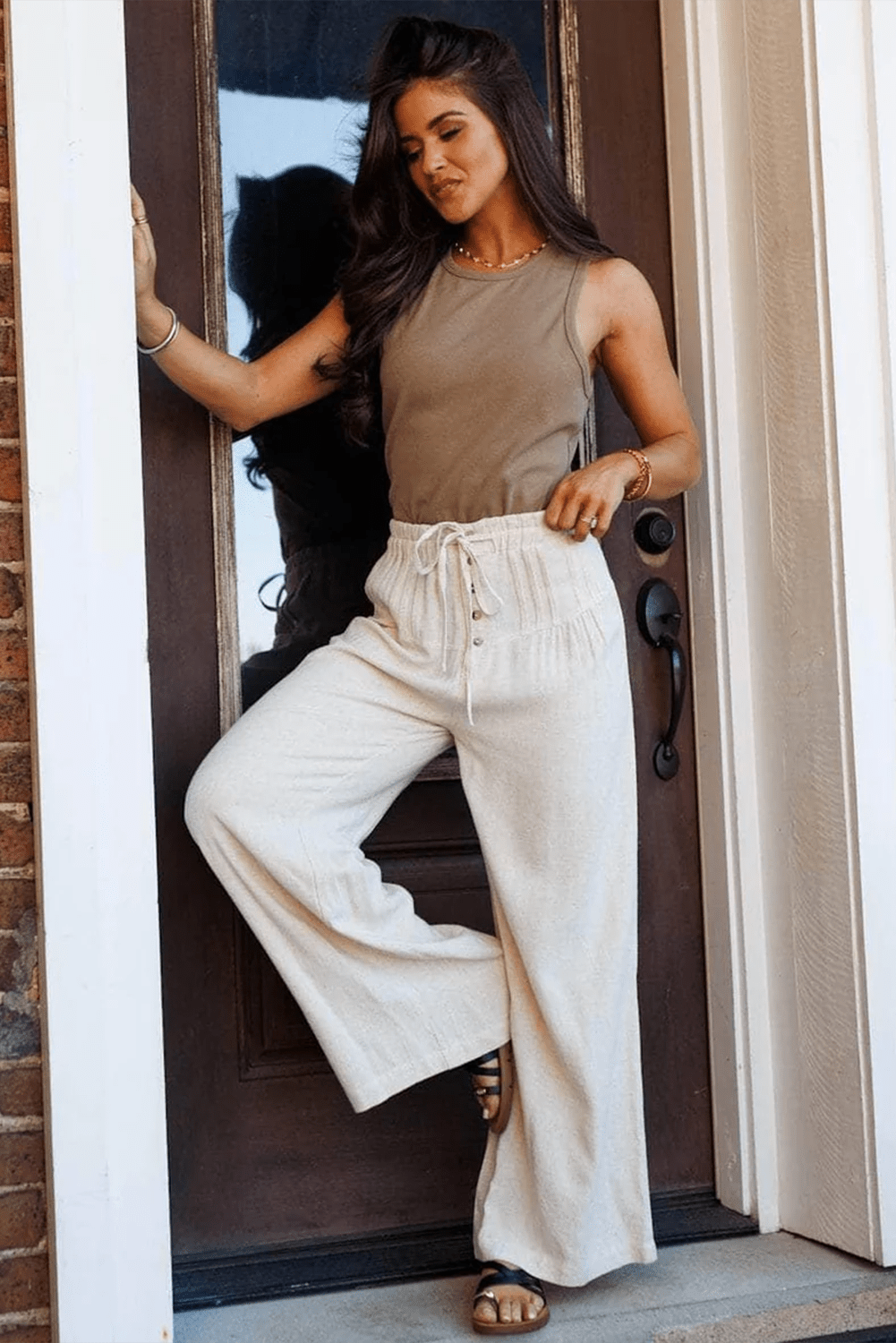 Woman in a brown top and white pants standing in a doorway.