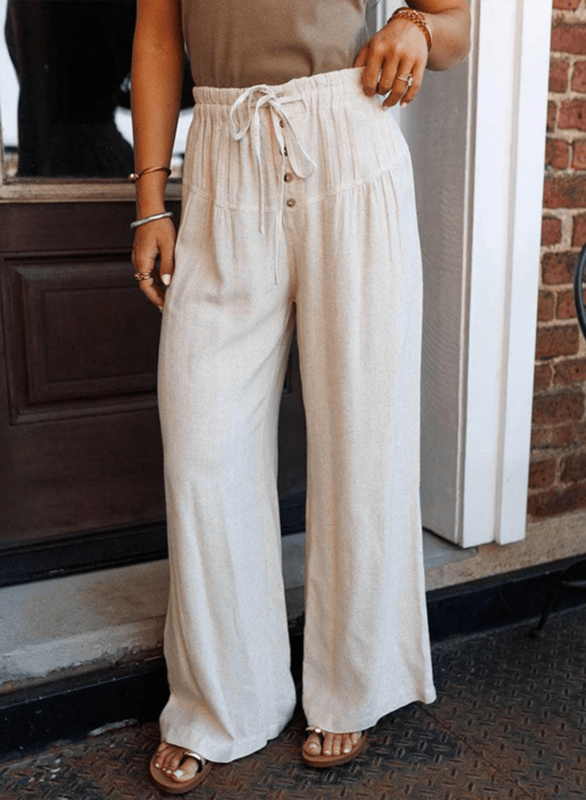Person wearing beige wide-leg pants with a brown top and sandals, standing on a step.