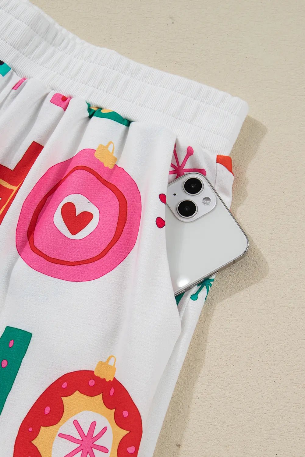 White shorts with colorful Christmas ornament print and smartphone in the side pocket.