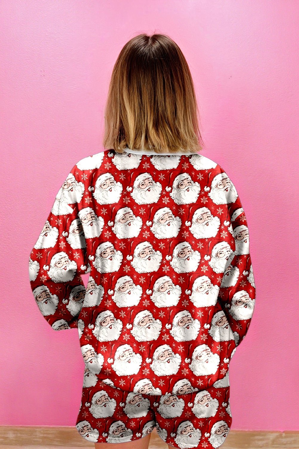 Person wearing a red pajama set with Santa Claus pattern against a pink background