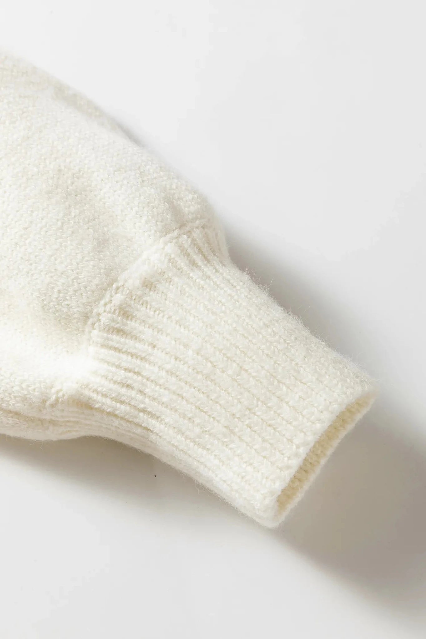 Close-up of a cream-colored knit garment sleeve with a ribbed cuff, shown on a clean white background.